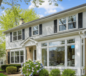 A two-story white house with large windows and a blooming hydrangea bush in the front yard in Schaumburg, IL by Midwest Windows, Siding & Doors