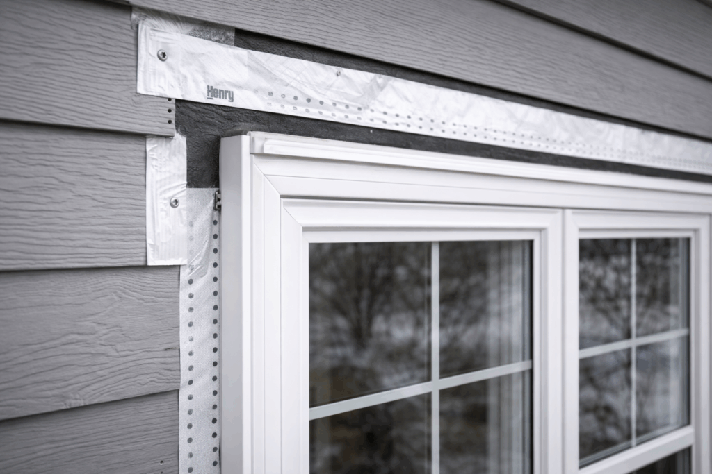 Close-up of properly flashed vinyl replacement window on Illinois home exterior, showing moisture barrier tape, tight trim fit, and gray horizontal siding alignment.