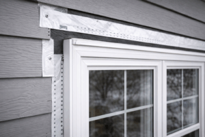 Close-up of properly flashed vinyl replacement window on Illinois home exterior, showing moisture barrier tape, tight trim fit, and gray horizontal siding alignment.